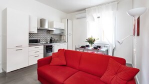 Une cuisine moderne avec des meubles blancs, un canapé rouge et un coin repas comprenant une table et des chaises.