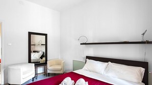 Une chambre d’hôtel avec un grand lit, une table de chevet, une chaise, un miroir et une étagère.