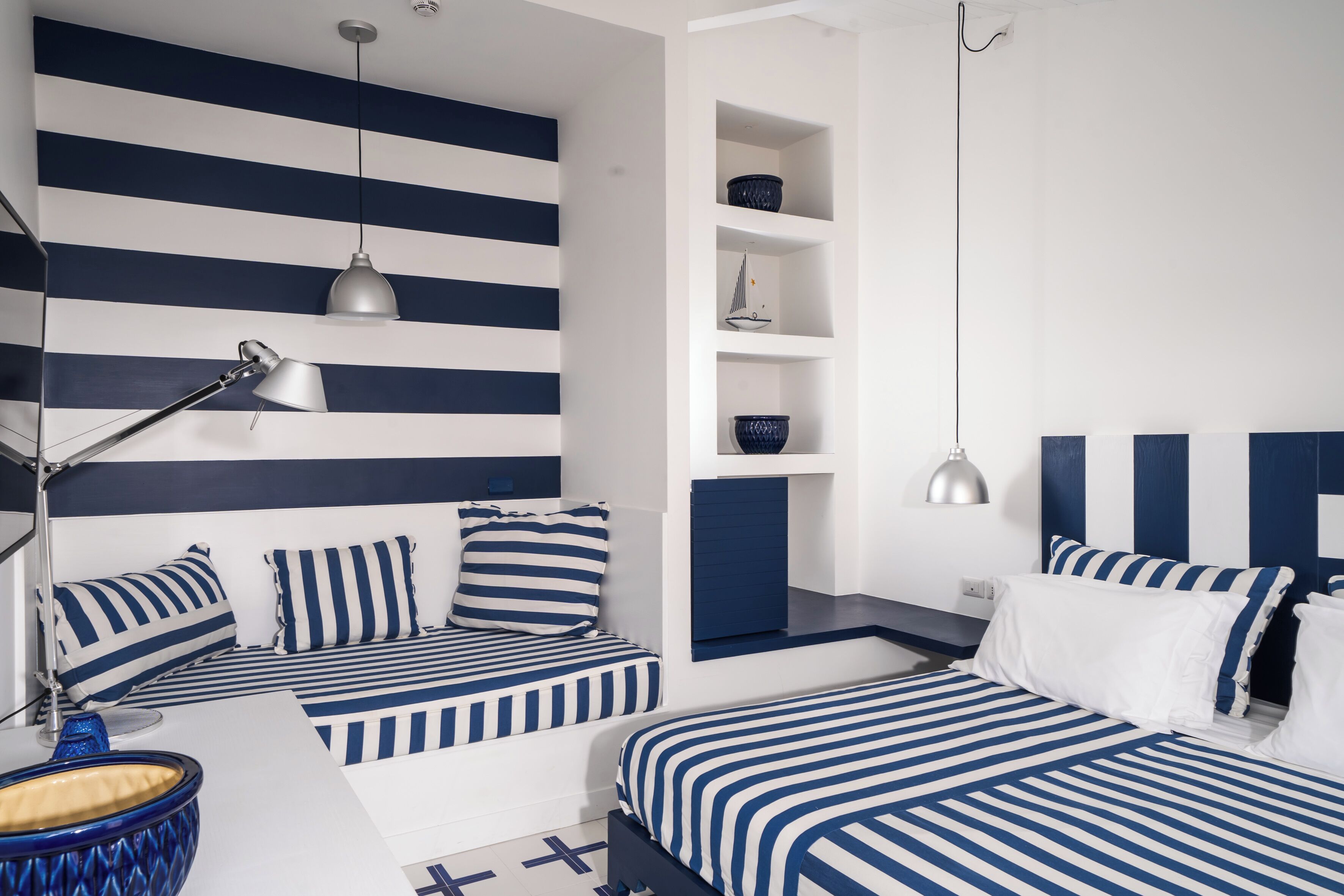 Un dormitorio moderno con ropa de cama azul y blanca a rayas, un escritorio con lámpara y estanterías empotradas.
