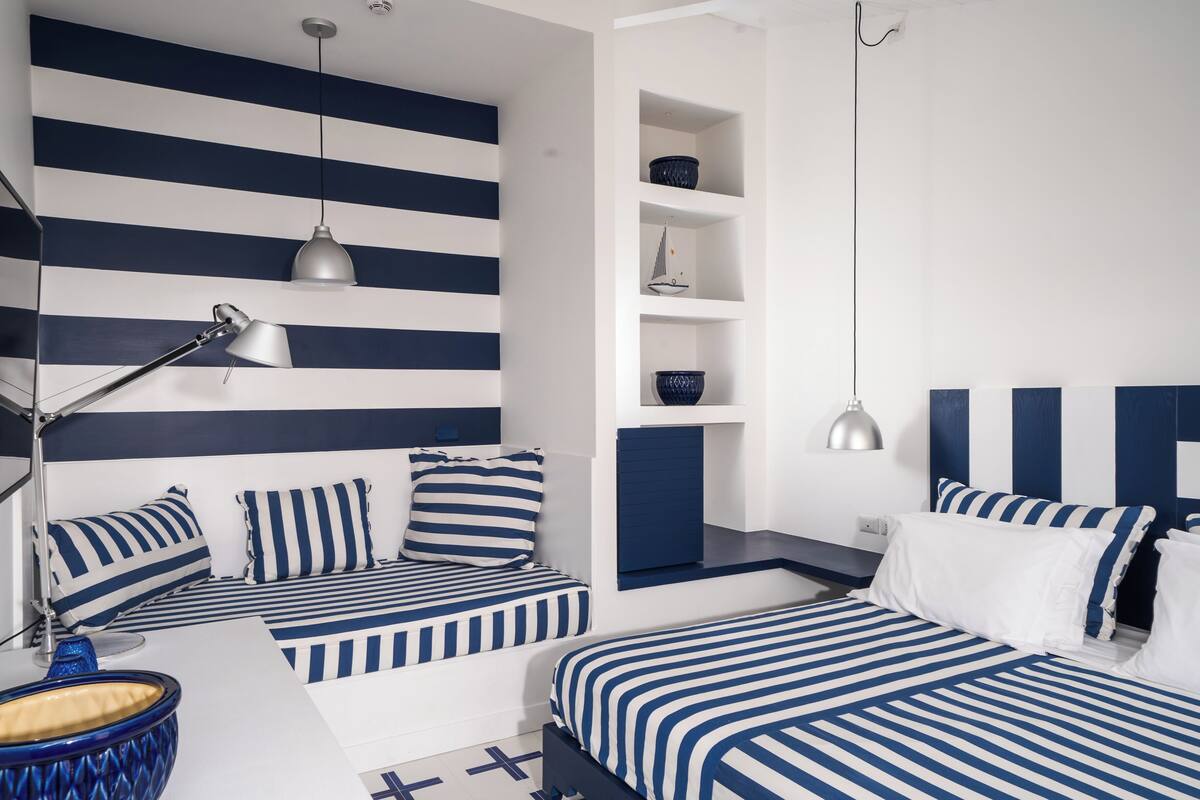 Un dormitorio moderno con ropa de cama azul y blanca a rayas, un escritorio con lámpara y estanterías empotradas.