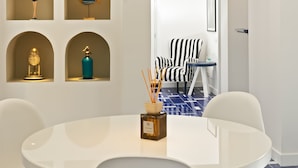 A modern dining area with a white round table and chairs, a blue pendant light, and shelves with decorative items. - Maison il Conservatorio (Sorrento)