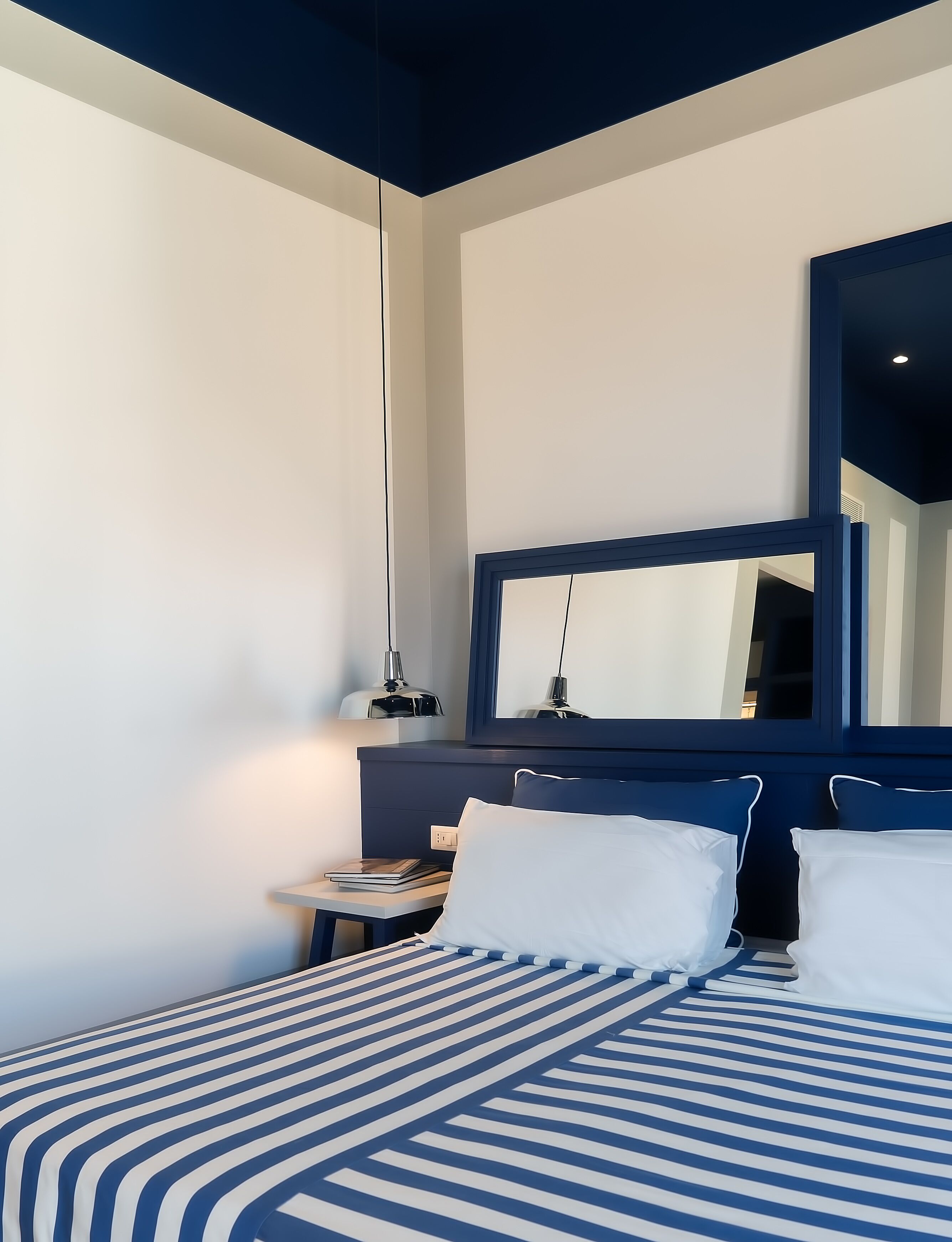 A modern hotel room with a large bed, a bedside table, a mirror, and a hanging lamp.