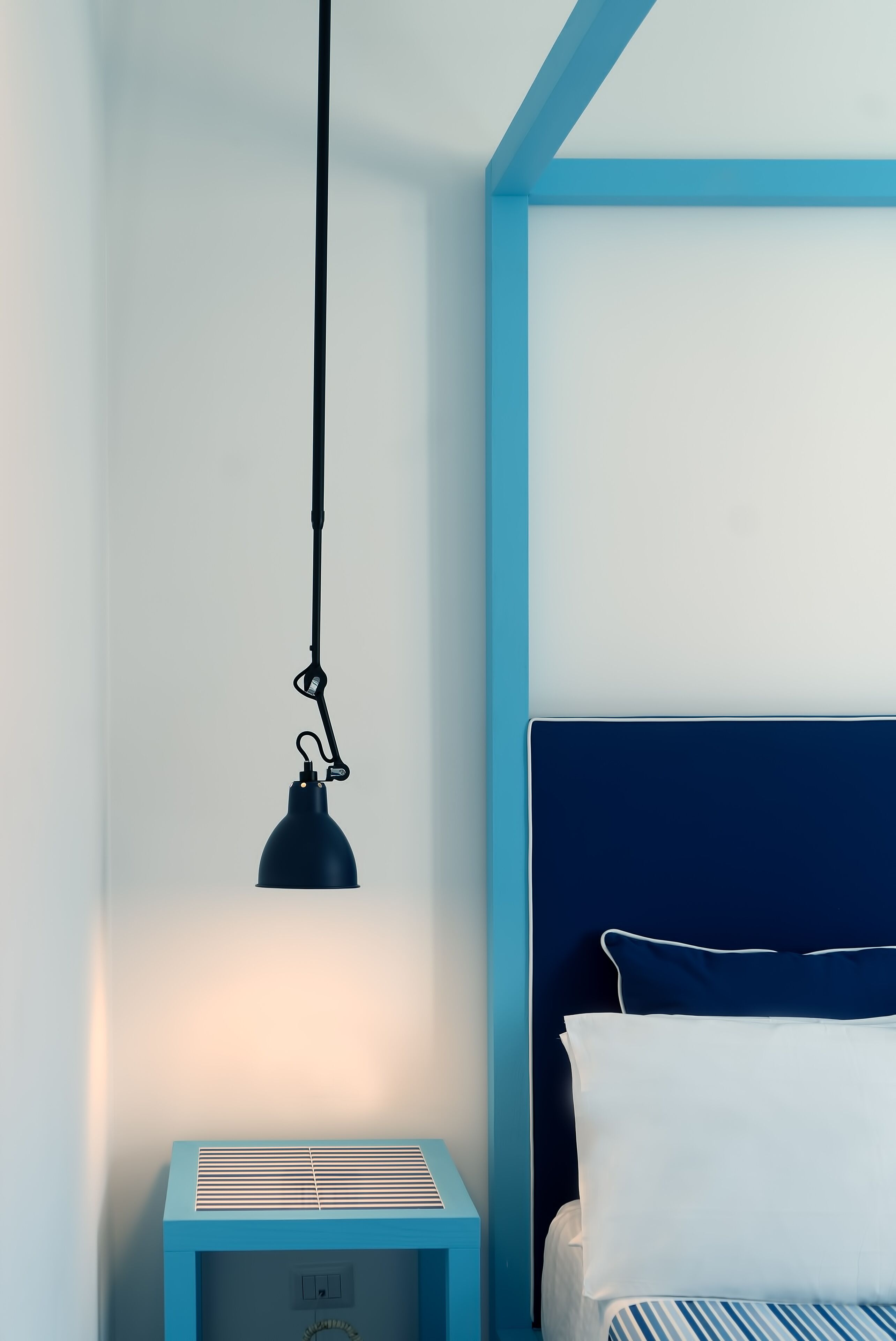 A bedroom with a bed, a bedside table, and a hanging lamp.