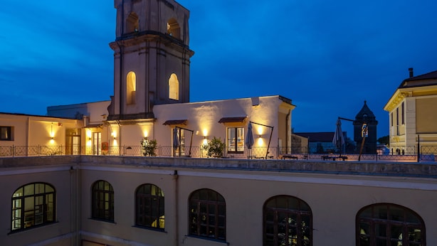 A historic building with a prominent tower and arched windows, featuring outdoor seating and a balcony with railings. - Maison il Conservatorio (Sorrento)