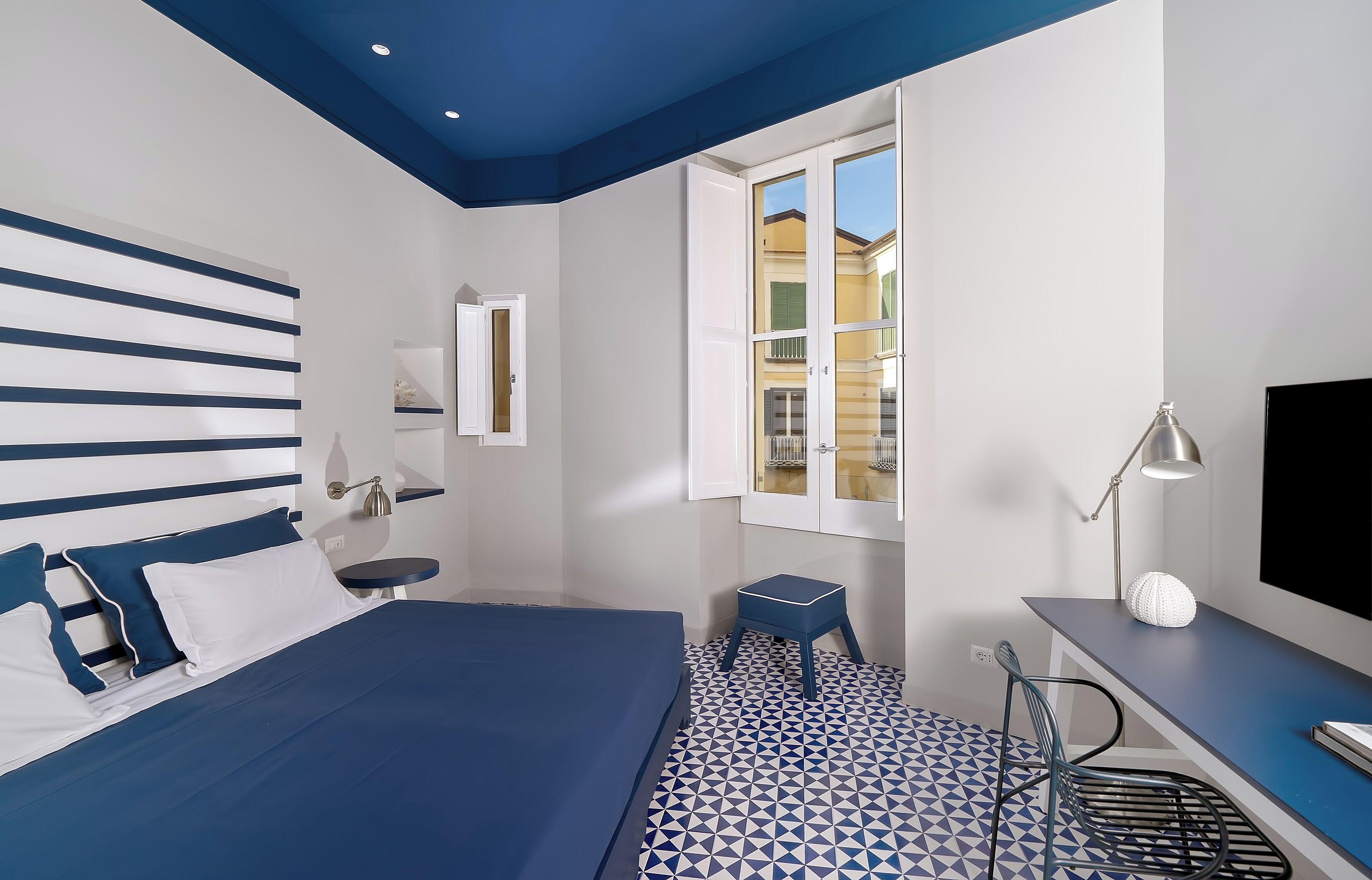 Un dormitorio con cama, escritorio, silla, ventana y televisor.