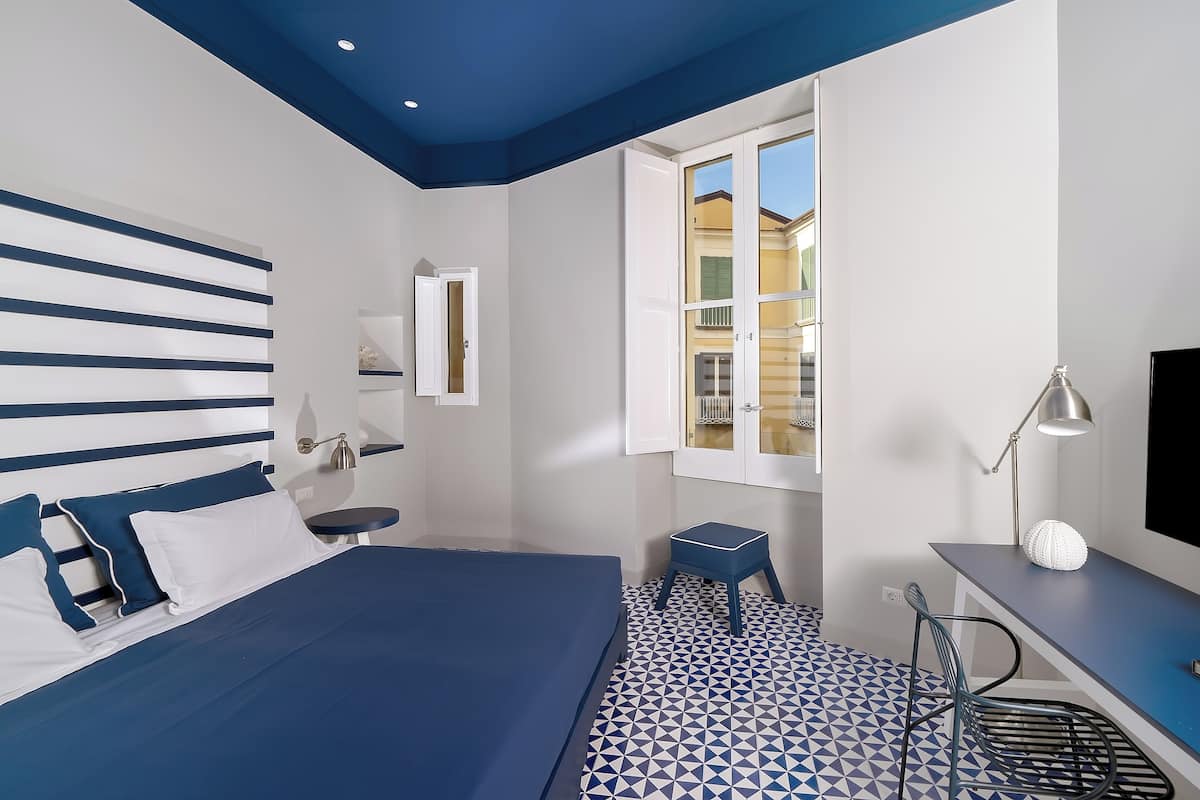 Un dormitorio con cama, escritorio, silla, ventana y televisor.