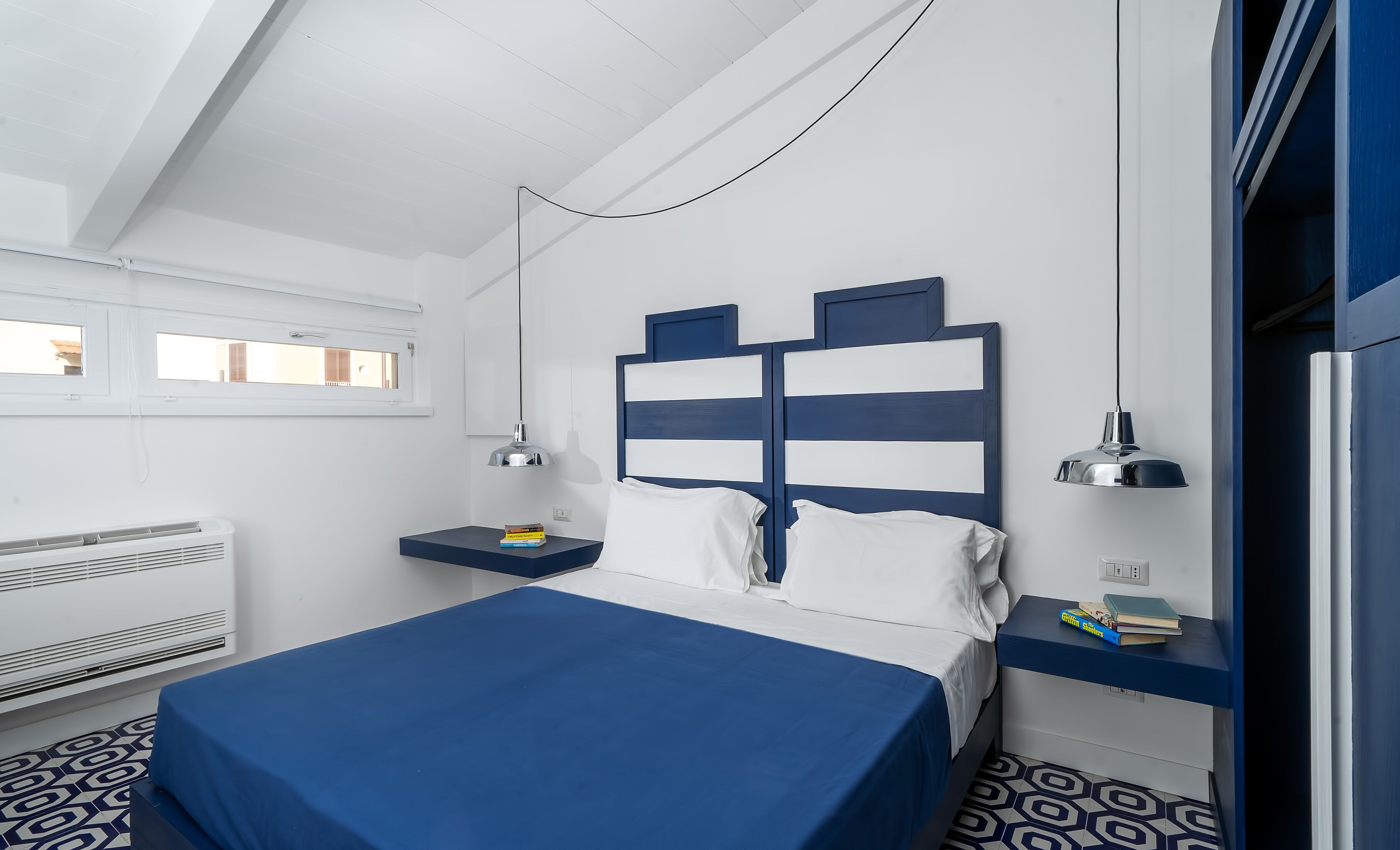 A modern bedroom with a bed, bedside tables, a window, and an air conditioning unit.