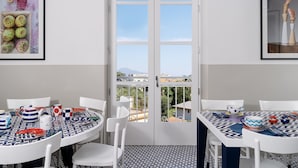 A dining area with white tables and chairs, a patterned floor, and a view through a glass door. - Maison il Conservatorio (Sorrento)