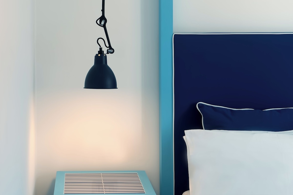 Un dormitorio con cama, mesita de noche y lámpara colgante.