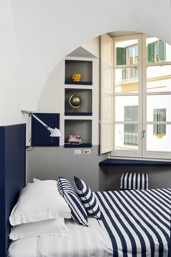 A bedroom with a bed, a desk with a lamp, a globe, and a window with shutters.