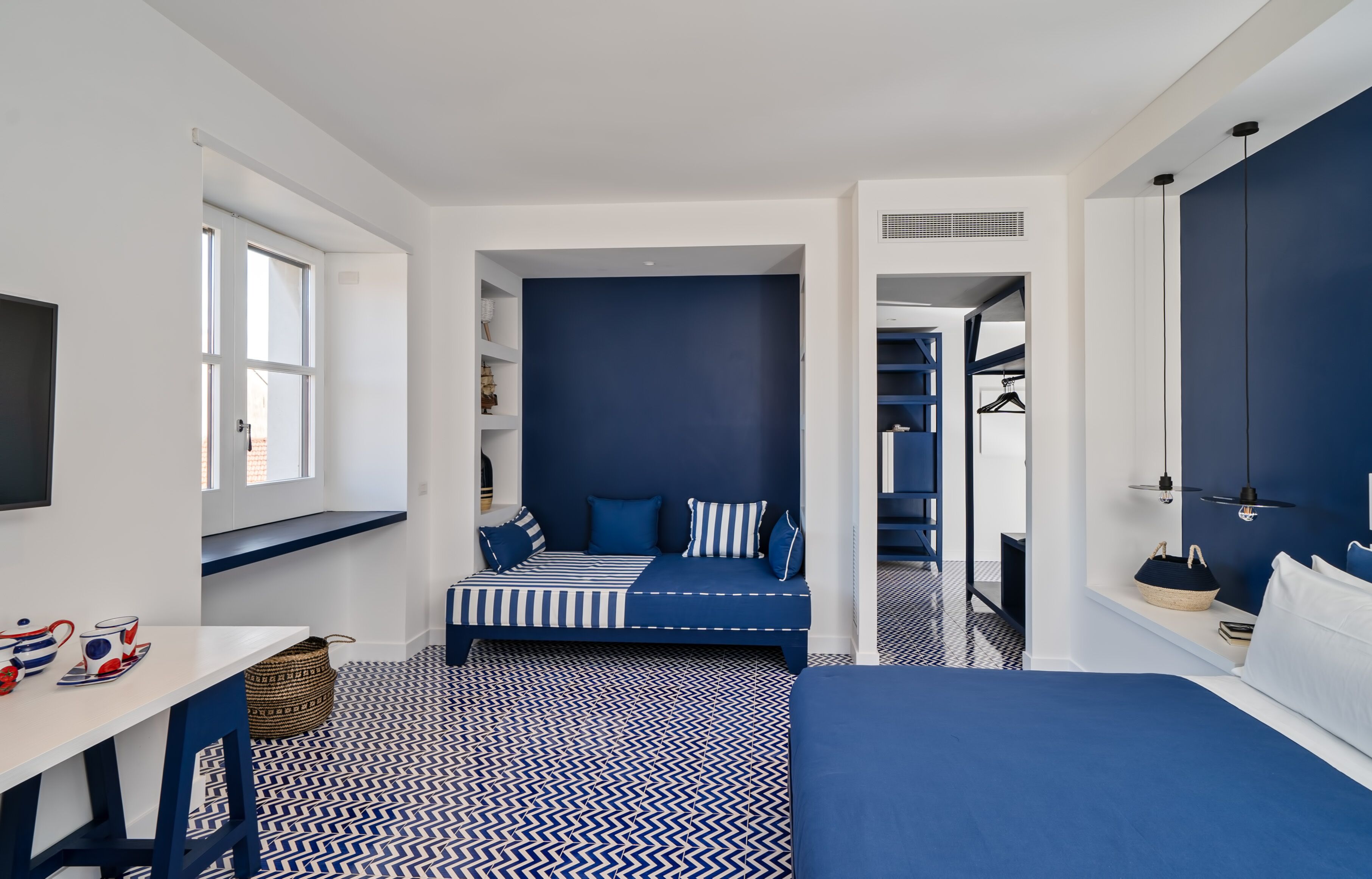 A compact room with a bed, a desk, and a seating area with a view of the outdoors.