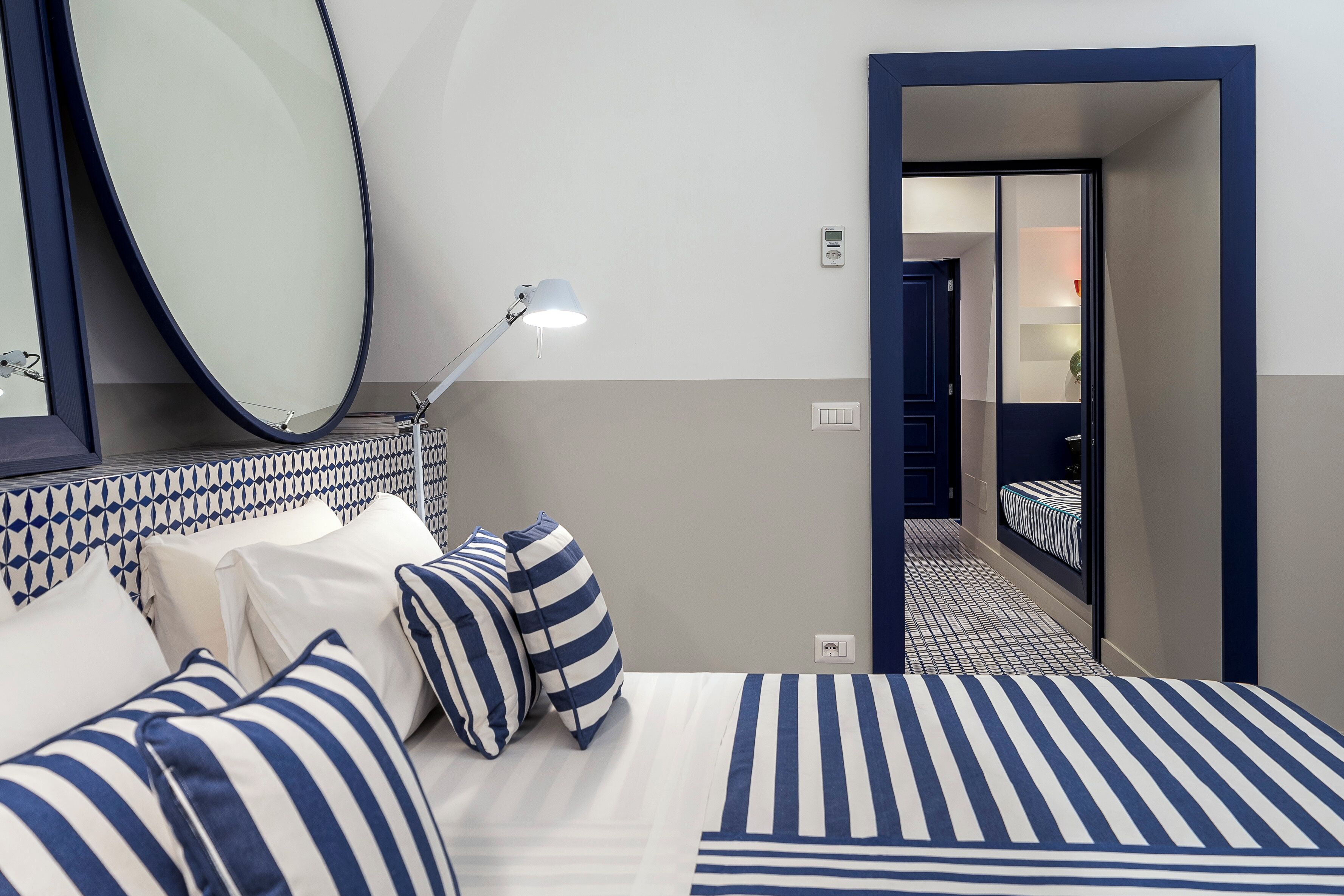 Une chambre d’hôtel avec un lit, un grand miroir, une lampe de chevet et une vue sur une autre chambre.