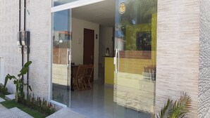 Un edificio moderno con entrada de vidrio, un área de comedor visible con sillas y una pared de ladrillo con un mural.