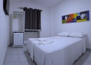 A hotel room with a bed, a small bedside table, a wardrobe, and a colorful abstract painting on the wall. - Jardins Premium (Ipojuca)