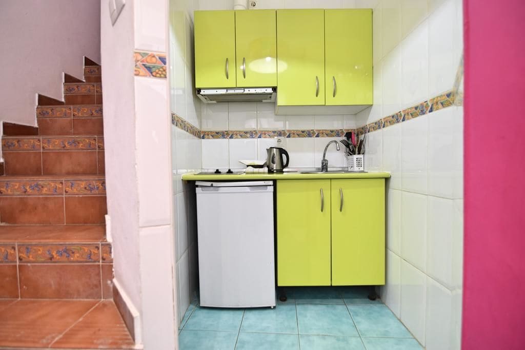Una cucina compatta con mobili verdi, lavastoviglie bianca e zoccolo in piastrelle.