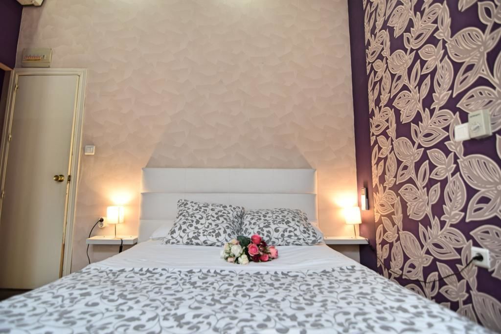 Una cama bien tendida con ropa de cama estampada, dos lámparas de noche y un diseño floral en la pared.