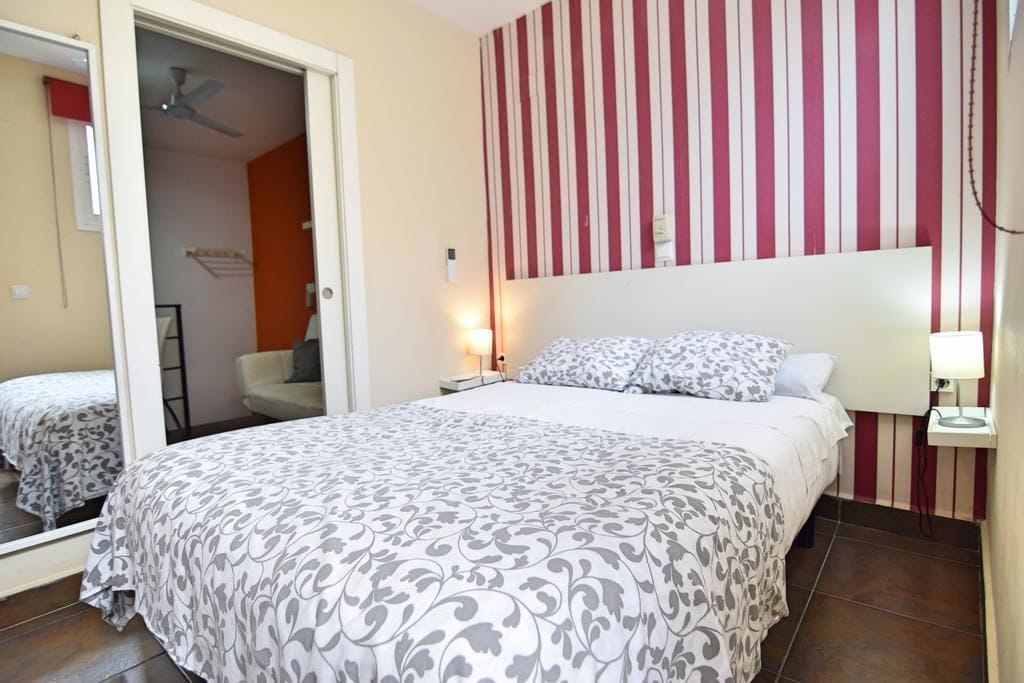 A bedroom with a bed, a nightstand, a mirror, and a striped wall.