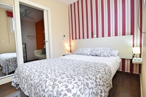 A bedroom with a bed, a nightstand, a mirror, and a striped wall. - Apartamentos Marqués de la Merced (Málaga)