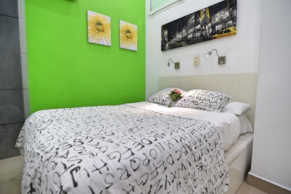 A bedroom with a green wall, a bed with a white and black patterned bedspread, two yellow flower wall art pieces, and a black and white cityscape painting above the bed.