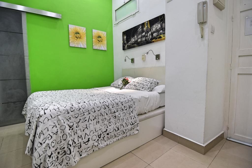 A bedroom with a bed, green walls, and two flower paintings.