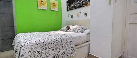A bedroom with a bed, green walls, and two flower paintings.