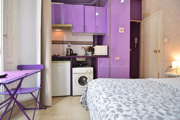 A compact room with a bed, a small table, a washing machine, and purple cabinets.