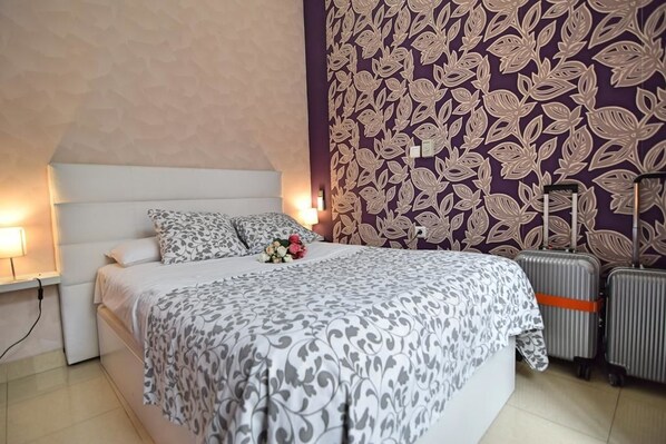 Una habitación de hotel con una cama, una mesita de noche, una lámpara, un papel tapiz con estampado floral y dos maletas.