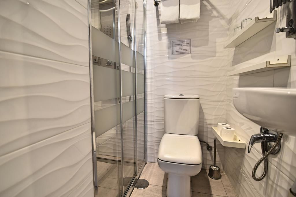 A modern bathroom with a glass-enclosed shower, a white toilet, and a sink with a handheld showerhead.