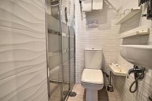 A modern bathroom with a glass-enclosed shower, a white toilet, and a sink with a handheld showerhead. - Apartamentos Marqués de la Merced (Málaga)
