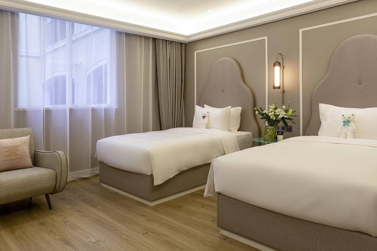 A hotel room with two beds, a sofa, a nightstand, and a window with curtains.