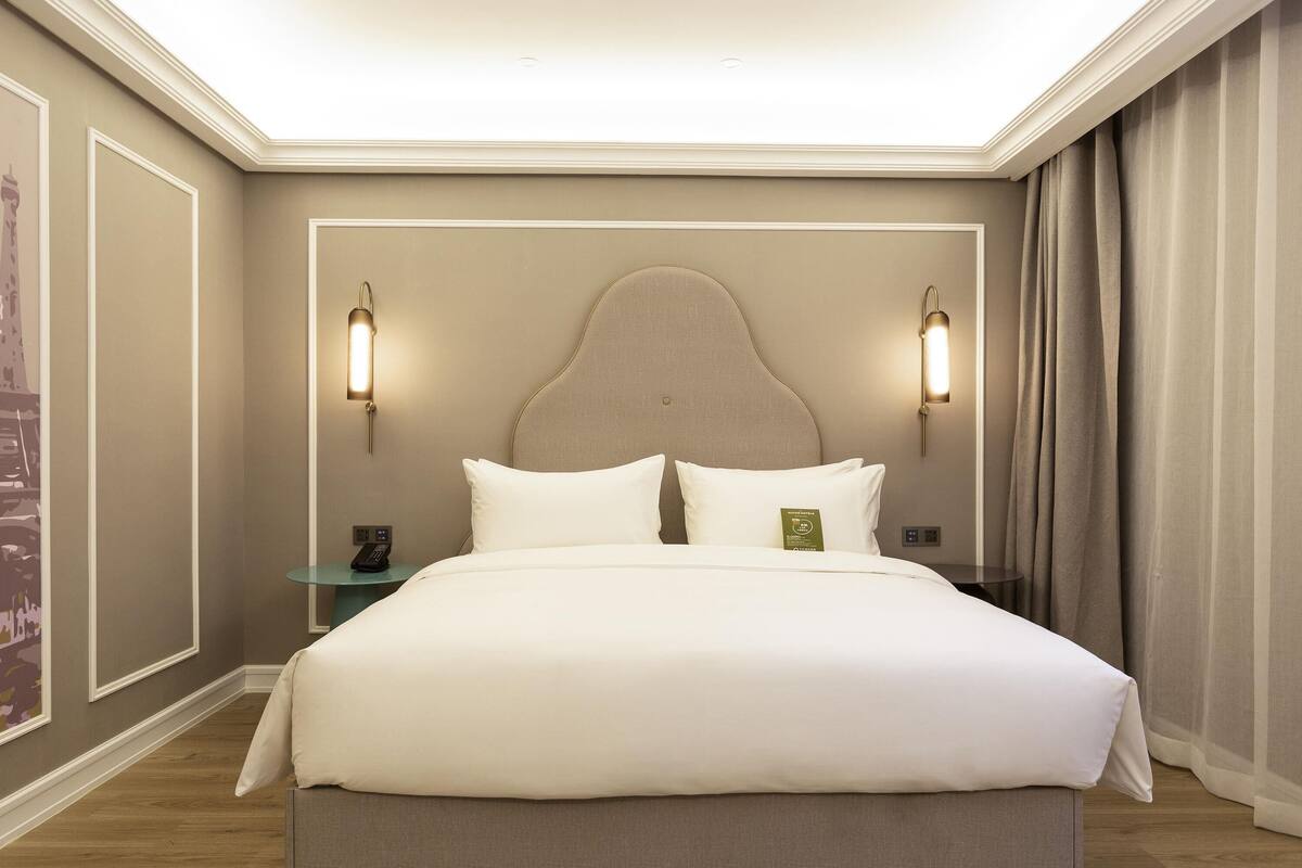 A large bed with a headboard, two bedside tables, and wall-mounted lighting.