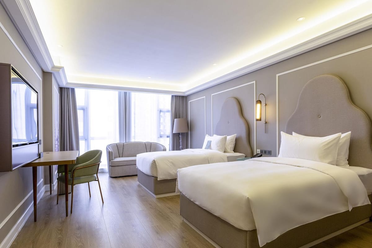 Habitación de hotel con dos camas, un escritorio, una silla y un televisor.