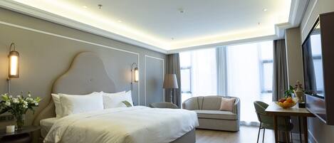 A modern hotel room with a large bed, a sofa, a dining table, and a TV.