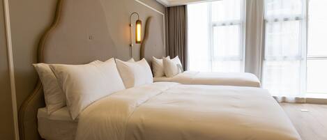 A hotel room with two beds, a large window, and a wall-mounted light fixture.