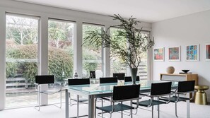 A modern dining area with a glass table, black chairs, and a large window with a view of greenery.