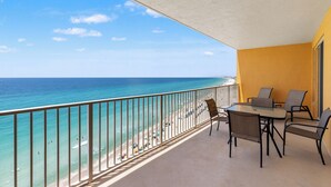 A balcony with a view of the beach and ocean, a table with chairs, and a yellow wall. - Treasure Island 1007 (Panama City Beach)