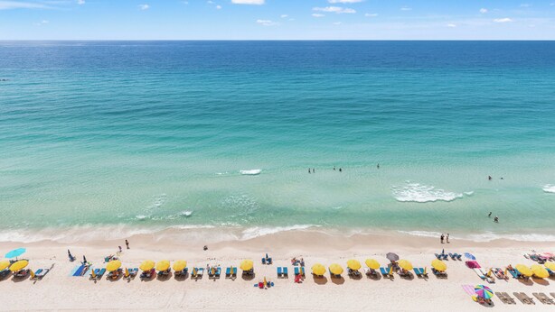 A beach with rows of sun loungers and umbrellas, a clear sky, and the ocean. - Treasure Island 1007 (Panama City Beach)