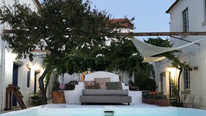 Ein Poolbereich mit einem weißen Pool, einer grauen Couch mit Kissen und umgebenden Topfpflanzen.