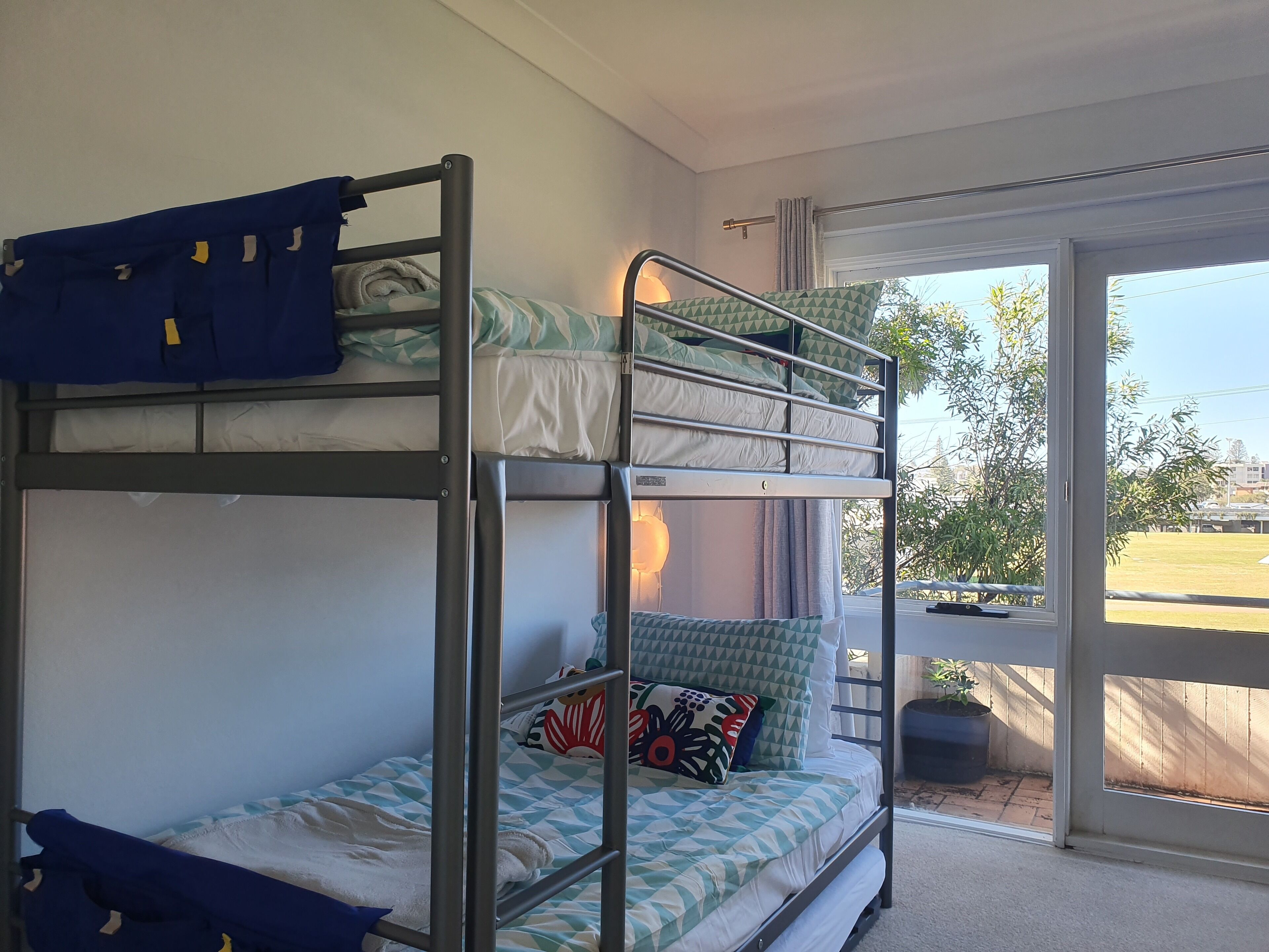 Une chambre avec des lits superposés donnant sur un jardin, visible à travers une porte vitrée.