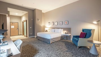 Une chambre d’hôtel comprenant un lit, un bureau, une chaise, une petite table et un mur orné de tableaux.