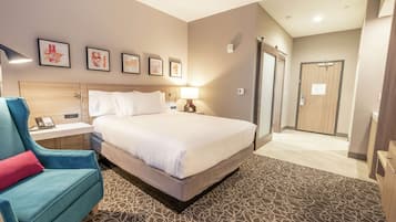 A hotel room with a bed, a desk with a phone, a chair with a red pillow, and a shower area.