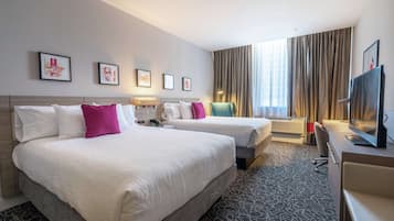 A hotel room with two beds, a desk, a TV, and artwork on the wall.