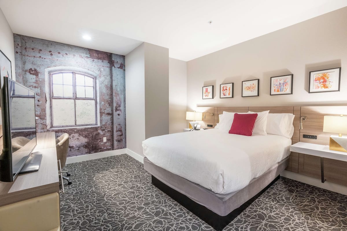 A hotel room with a large bed, a desk, a chair, and a wall mural.