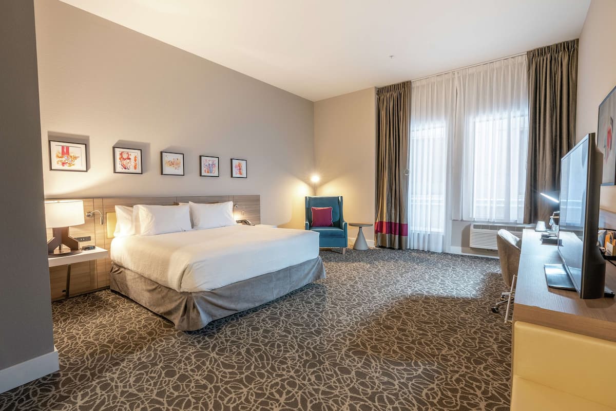 A hotel room with a large bed, a desk, a chair, a TV, and framed artwork on the wall.