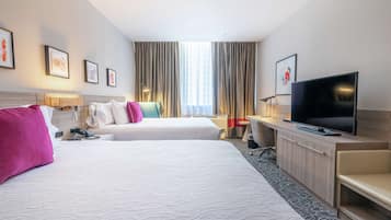 A hotel room with two beds, a TV, a desk, and a window with curtains.