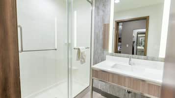 Un baño moderno con cabina de ducha de vidrio, un lavamanos blanco y un mueble de tocador de madera.