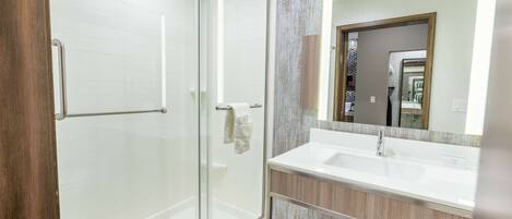 A modern bathroom with a glass shower enclosure, a white sink, and a wooden vanity.