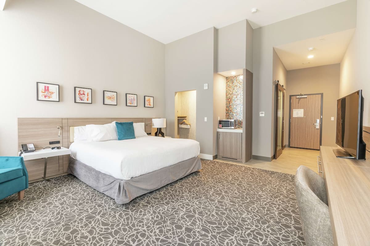A modern hotel room with a large bed, a desk, a chair, a TV, and a bathroom visible through an open door.