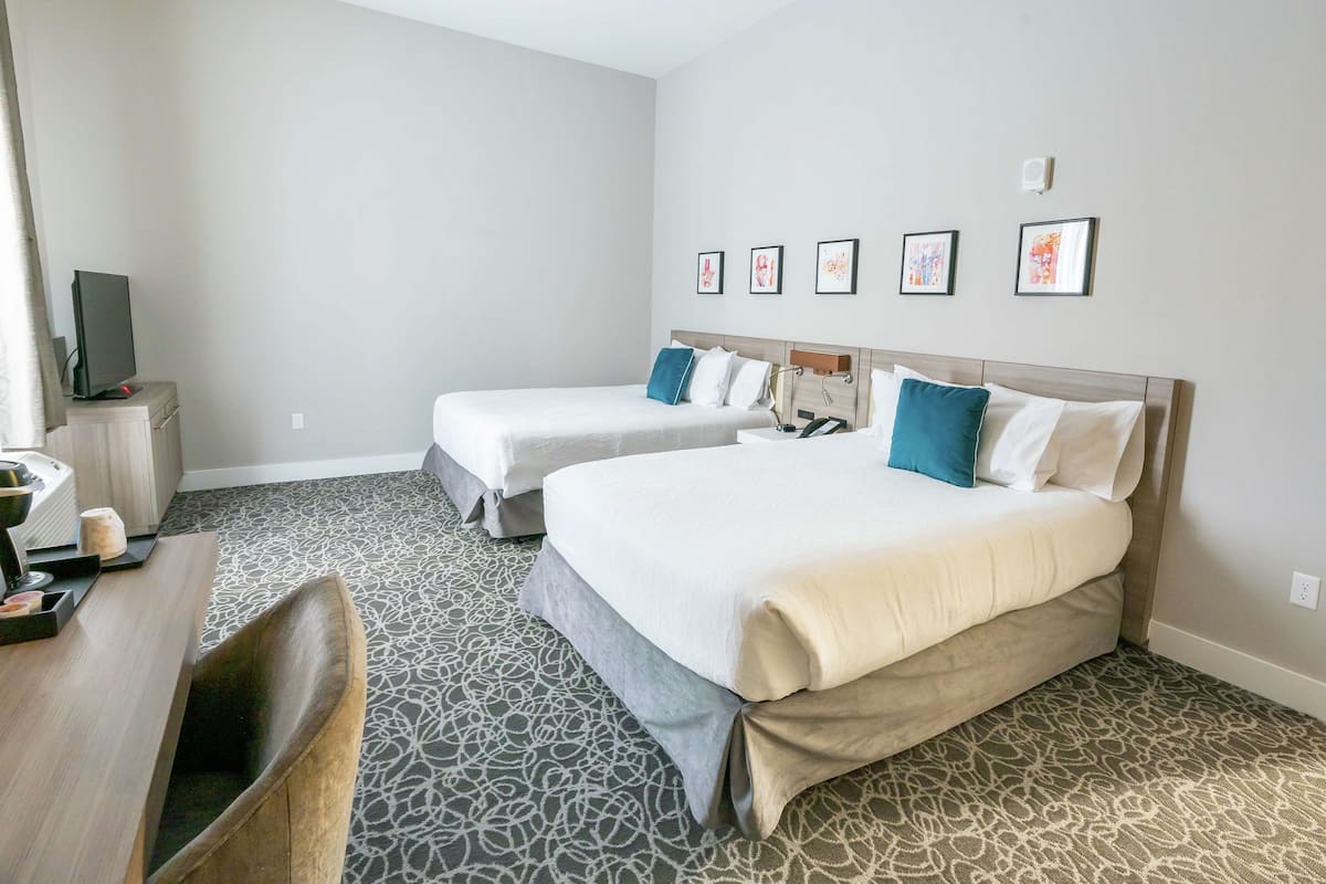 A hotel room with two beds, a desk, and a television.
