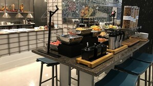 Een buffetopstelling met diverse etenswaren en bestek, een toonbank met krukken, en een decoratieve spatwand.